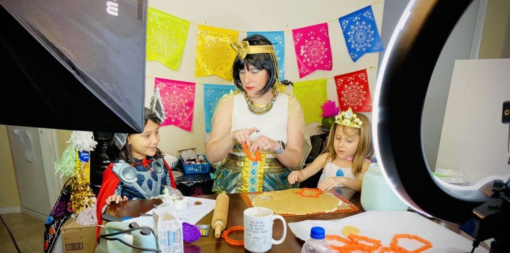 A woman dressed as Cleopatra making cookies with a child dressed as Thor and a child dressed as a princess