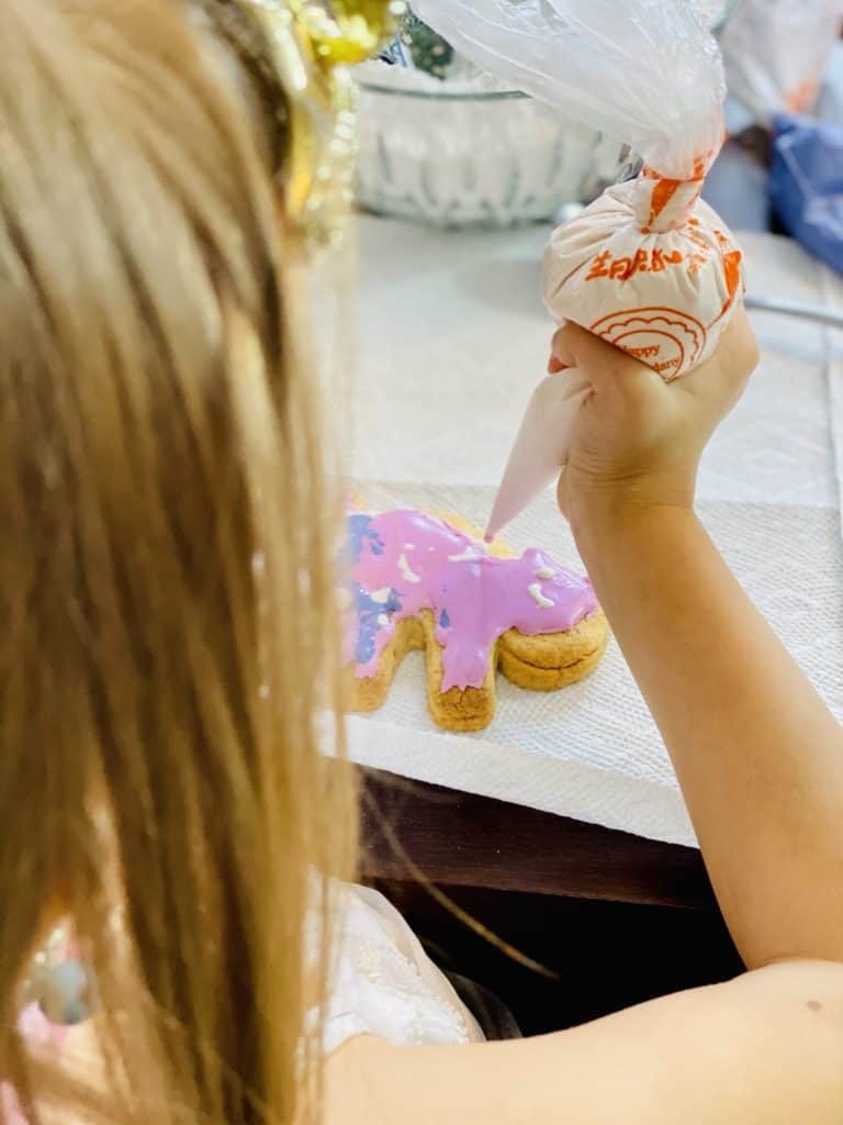 A child with blonde hair decorating a cat shaped cookie, viewed from behind