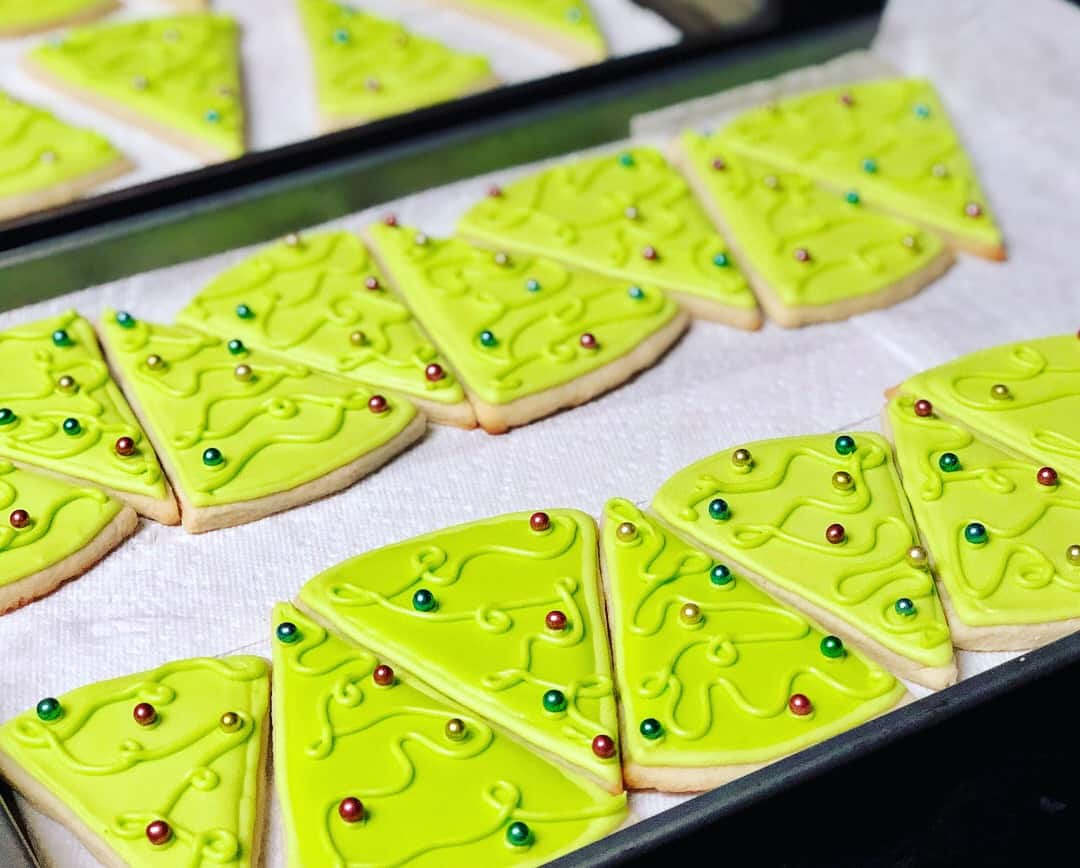 Bright green Christmas tree sugar cookies lined up on a baking tray, with different colored sugar pearls as ornaments.