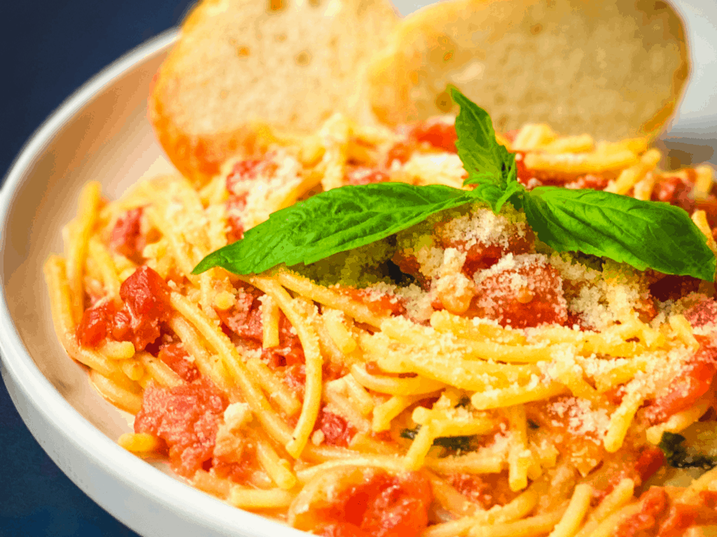 close up of spaghetti and tomato cream sauce, garnished with fresh basil leaves and slices of bread