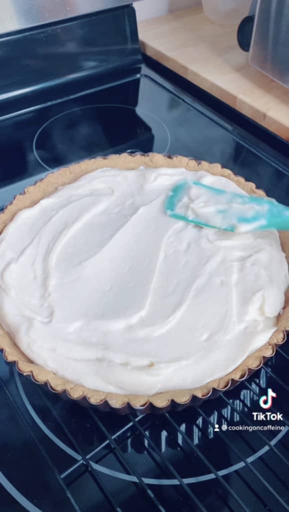 smoothing the cheesecake filling with a blue spatula which has been poured into a graham cracker pie crust
