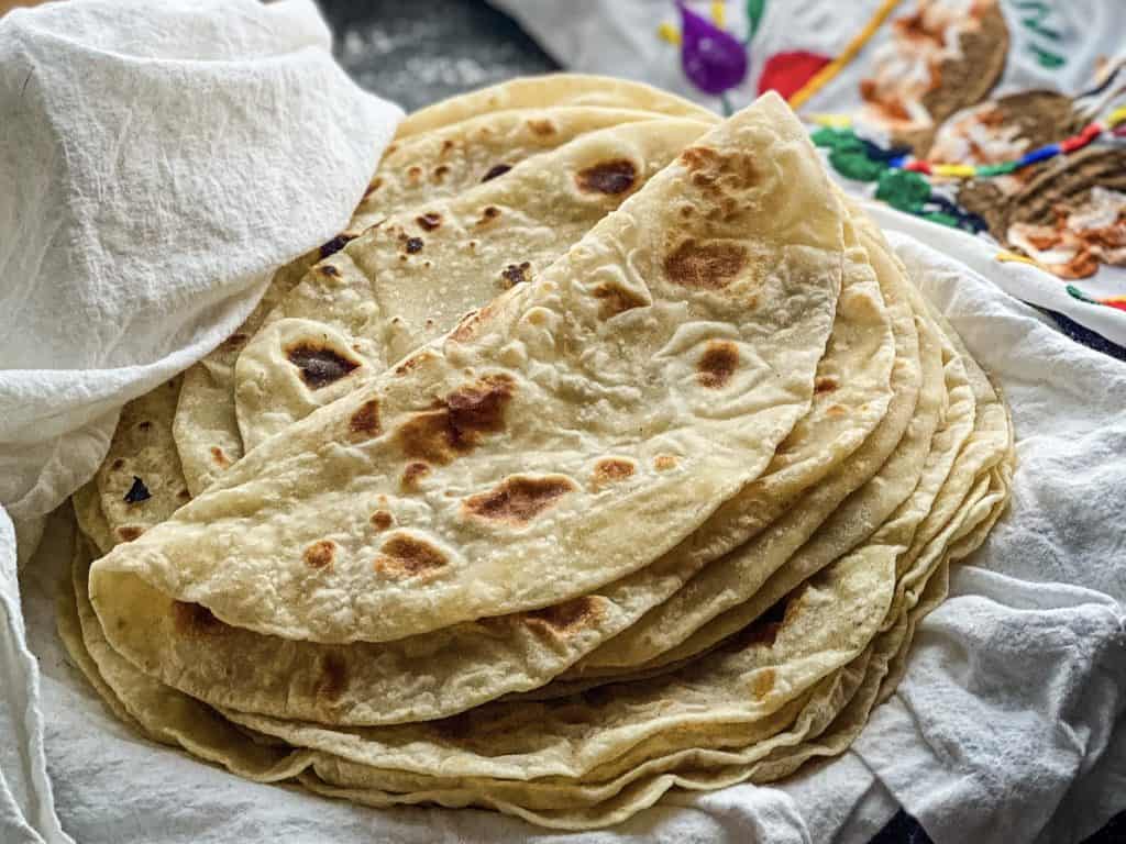 A stack of fresh tortillas sitting on a white cloth