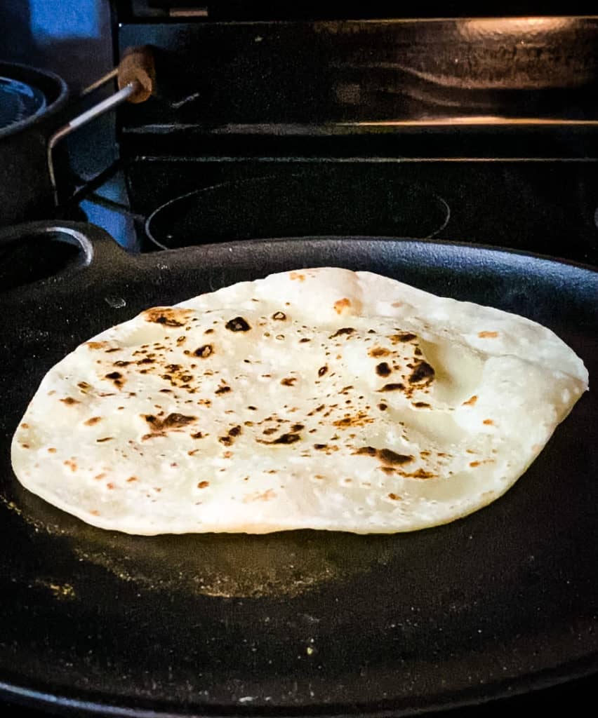 A flipped tortilla in a skillet with dark spots and some bubbles forming