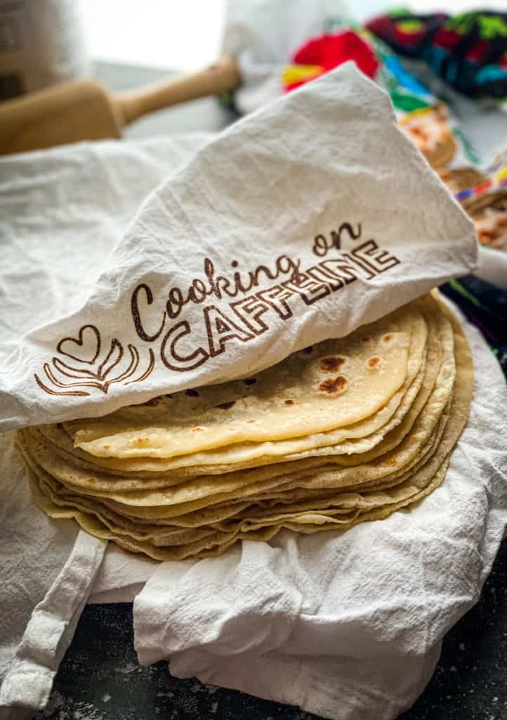 a stack of fresh tortillas wrapped in a white cloth branded with cooking on caffeine