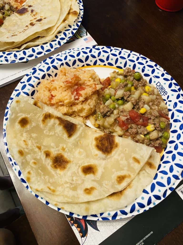 A paper plate with tortillas, mexican rice, and picadillo