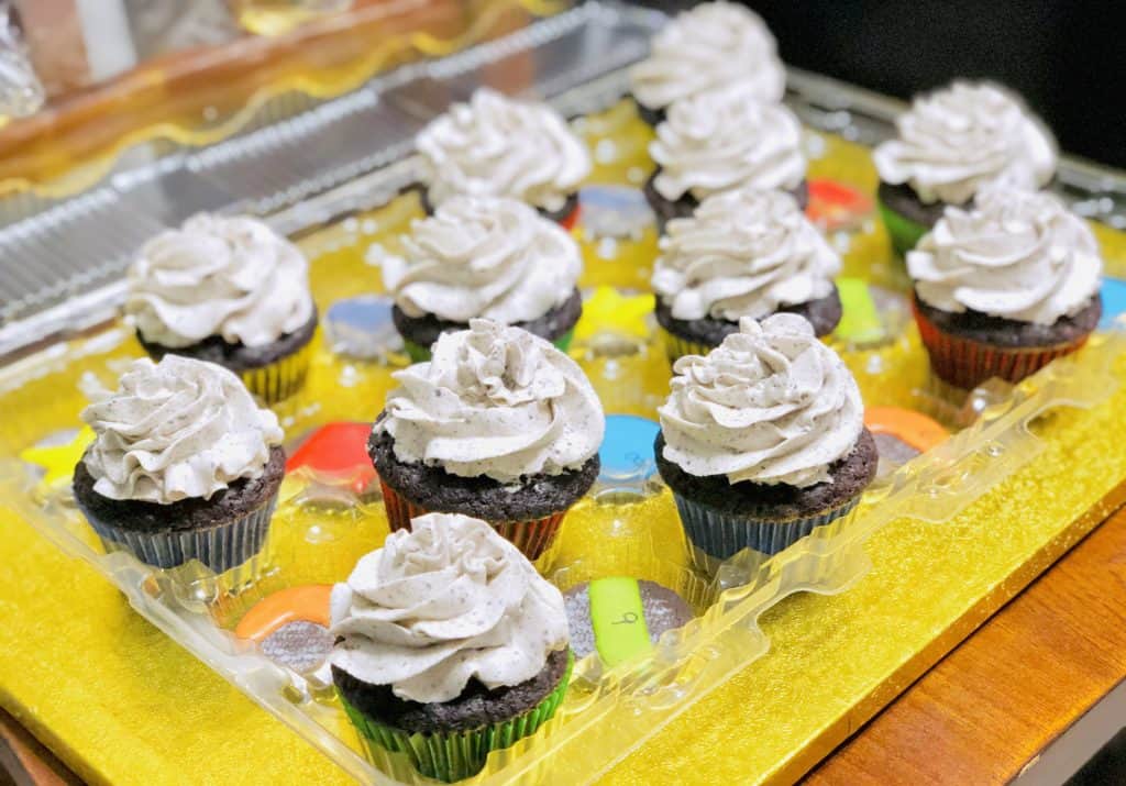 a plastic container full of cookies and cream cupcakes with traditional cupcake swirls of frosting on top