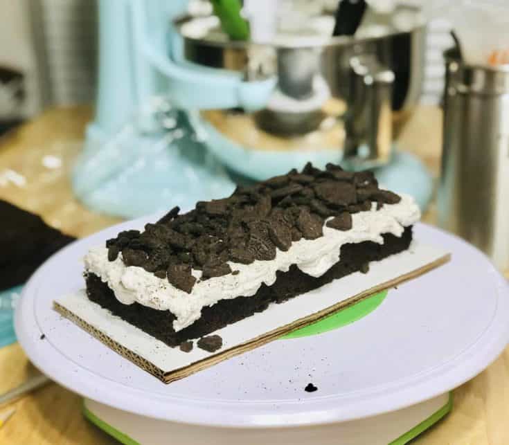 a rectangular chocolate cake with speckled white buttercream on top and oreo cookie shards on top of that
