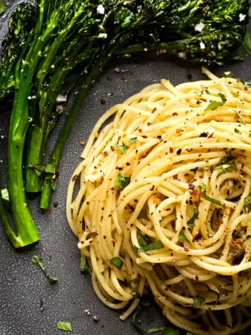 a swirl of spaghetti on a grey plate, nestled by broccolini.