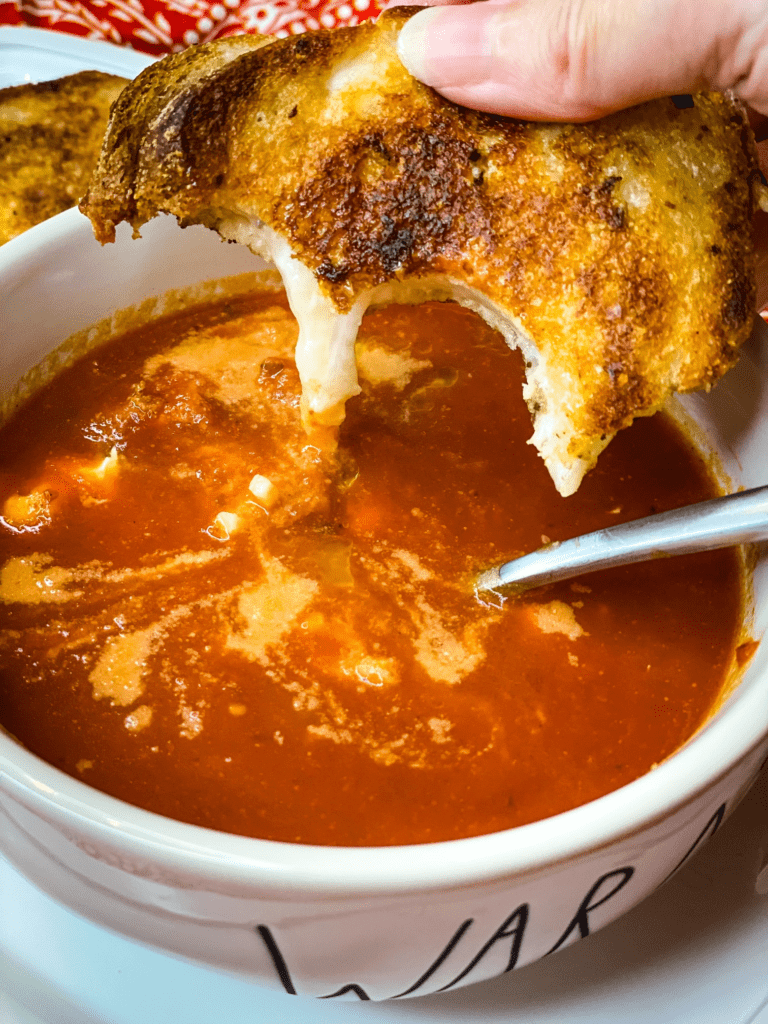 dipping a crispy grilled cheese sandwich into some tomato soup with a healthy serving of parmesan cheese on top