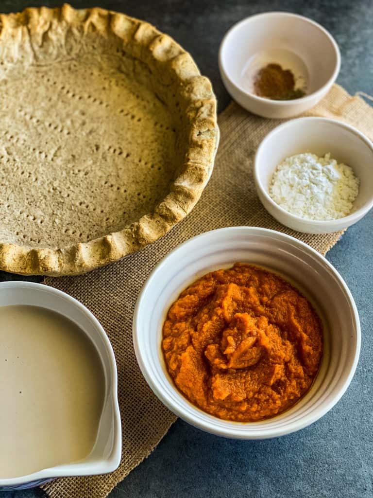 Photo of the ingredients for the perfect vegan pumpkin pie: a pie crust, coffee creamer, pumpkin puree, cornstarch, and spices