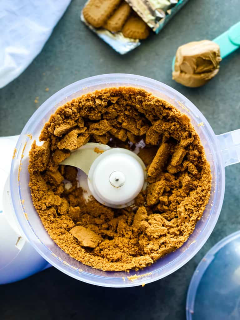 Biscoff cookies are blended up about 50% in the bowl of a food processor