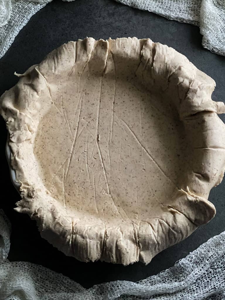the raw gluten free pie crust fully pressed into the pie pan with the edges overflowing the sides