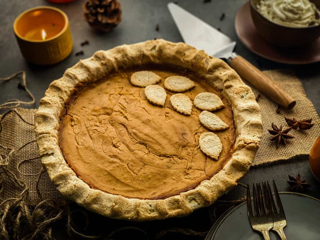 the finished pumpkin pie with leaf decorations made out of extra crust, surrounded by a set table ready to eat