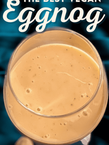 Looking down into a wine glass full of thick, delicious eggnog. It's sitting on peacock blue satin with two nutmeg pods at the base. The overlay reads The best vegan eggnog, creamy custardy and convincing
