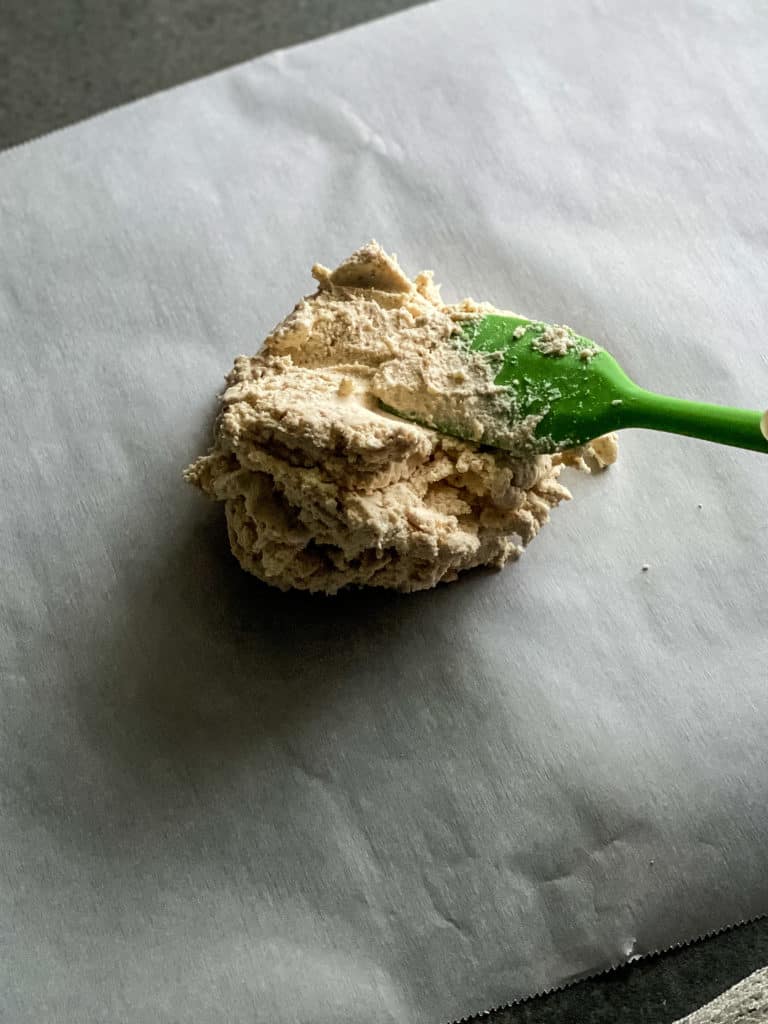 a ball of dough placed onto a large sheet of parchment paper with a green spatula