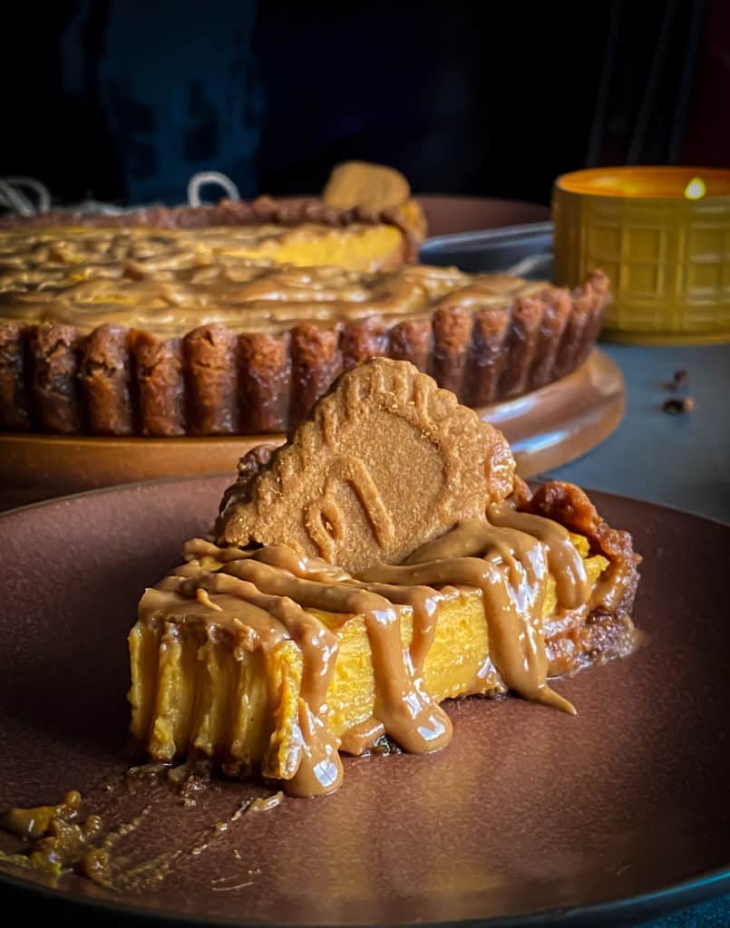 A front on look at a slice of pumpkin cookie butter cheesecake with a forkful taken and a biscoff lotus cookie on top