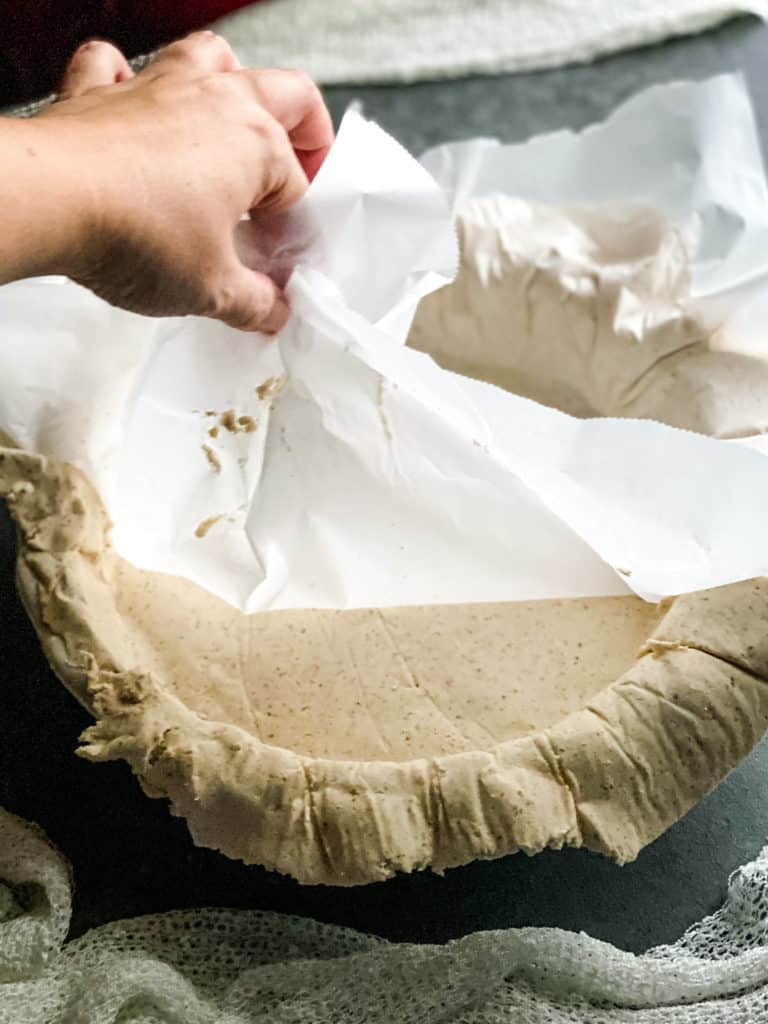 peeling the layer of parchment off the pie crust which has been pressed into the greased pie plate