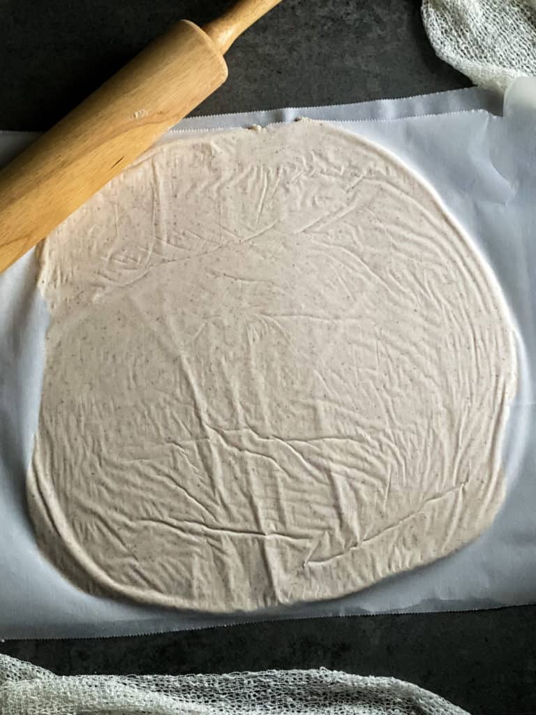 a large circle of dough that has been rolled out between two sheets of parchment paper