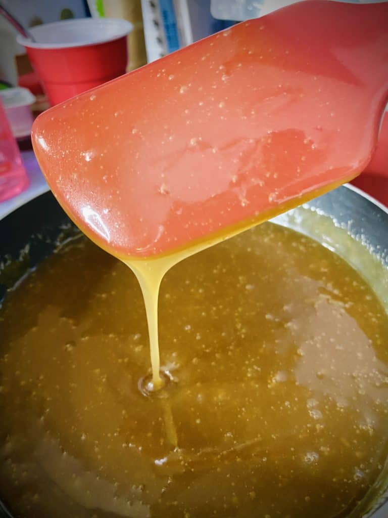 Golden caramel pouring off a red spatula in a long ribbon.