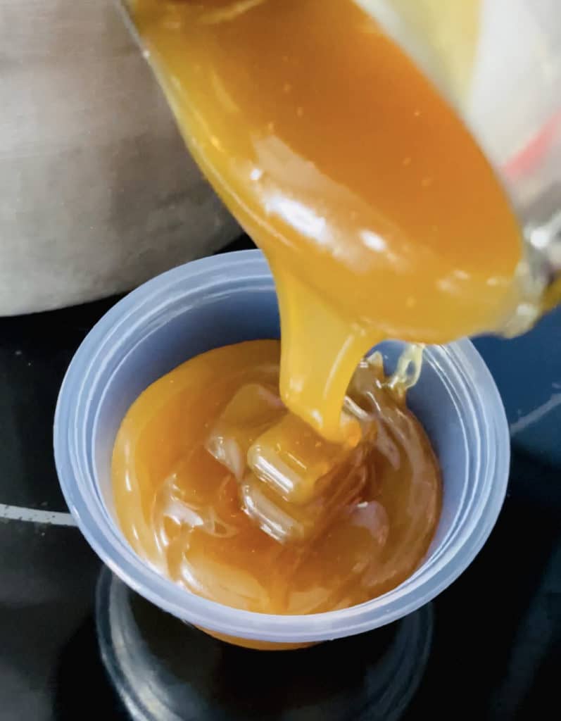 An ice cream scoop portioning out caramel into a small plastic container
