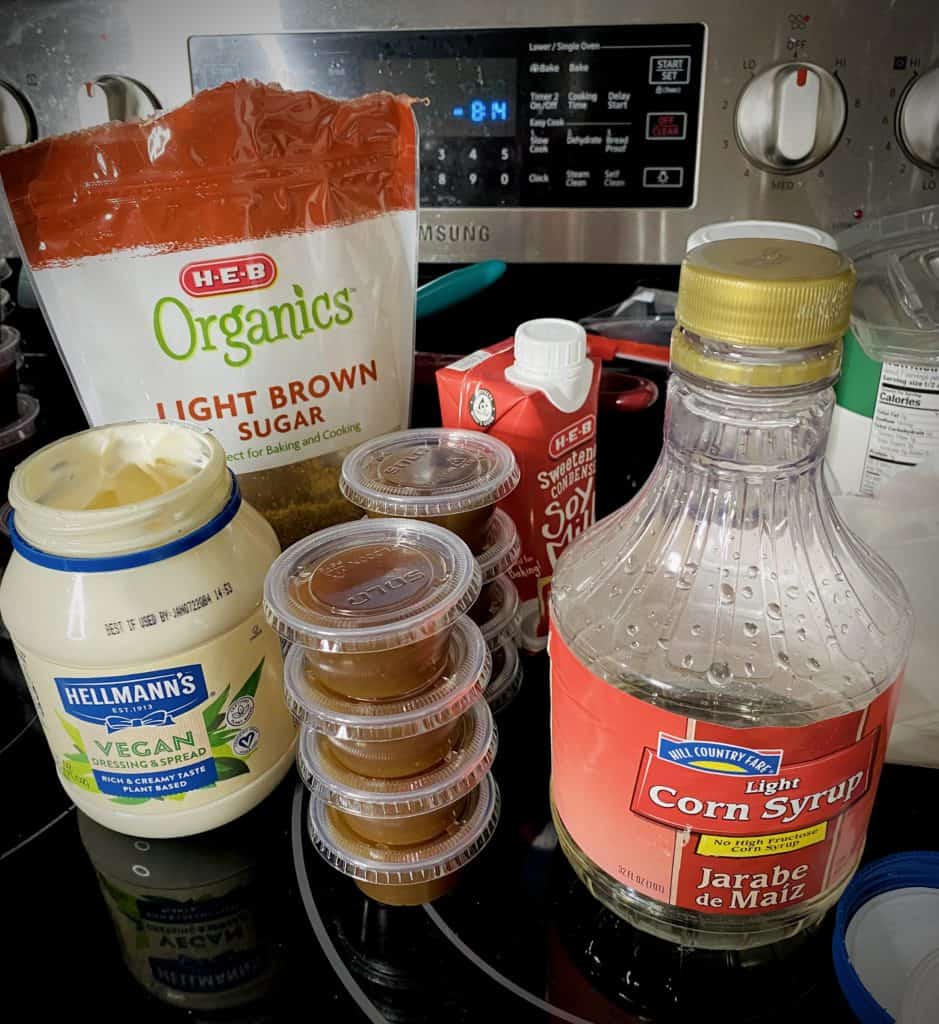 Corn syrup, vegan mayonnaise, organic brown sugar, sweetened condensed soy milk, and eight small containers of finished caramel sitting on a stove.