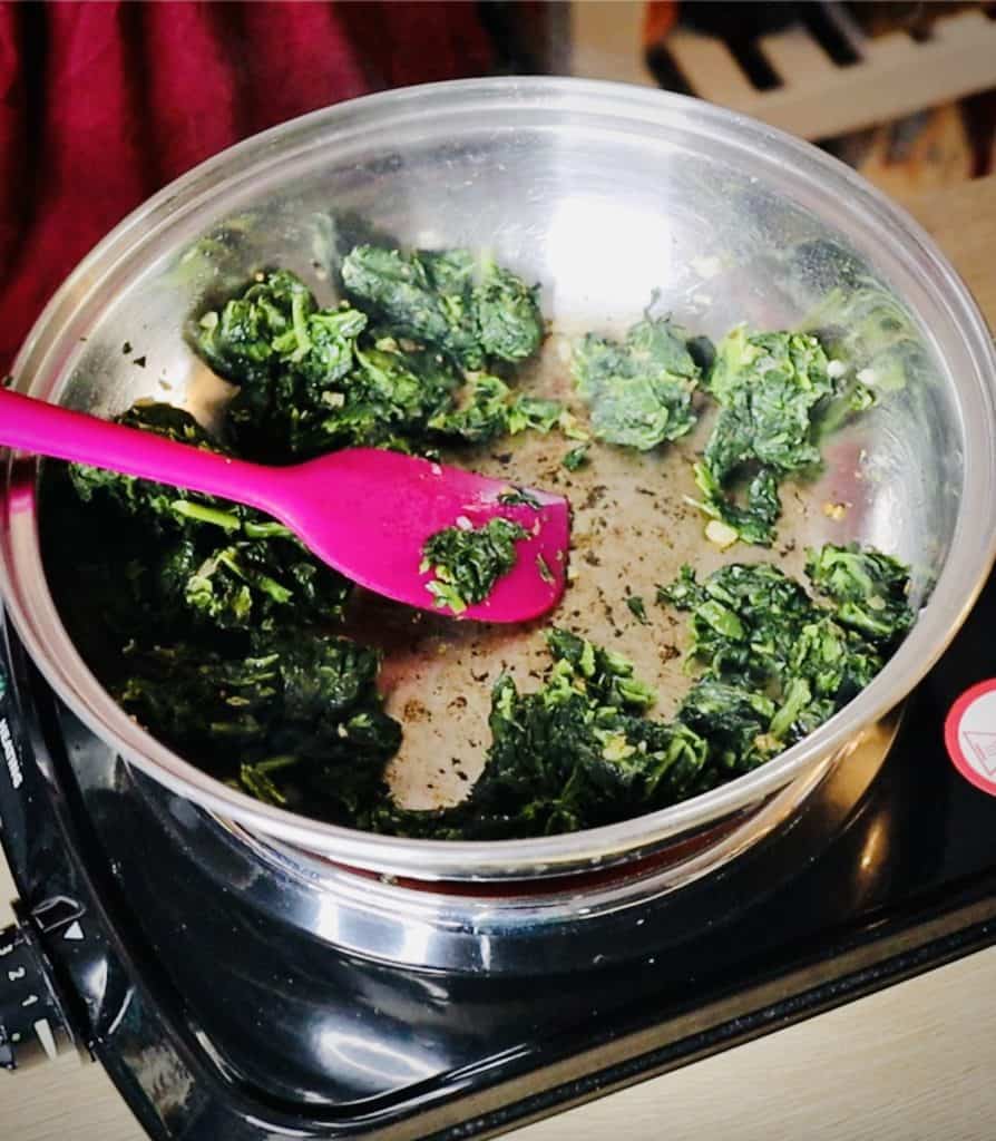 Dry clumps of deep green spinach in a stainless steel saute pan with the bottom of the pan having brown caramelized bits