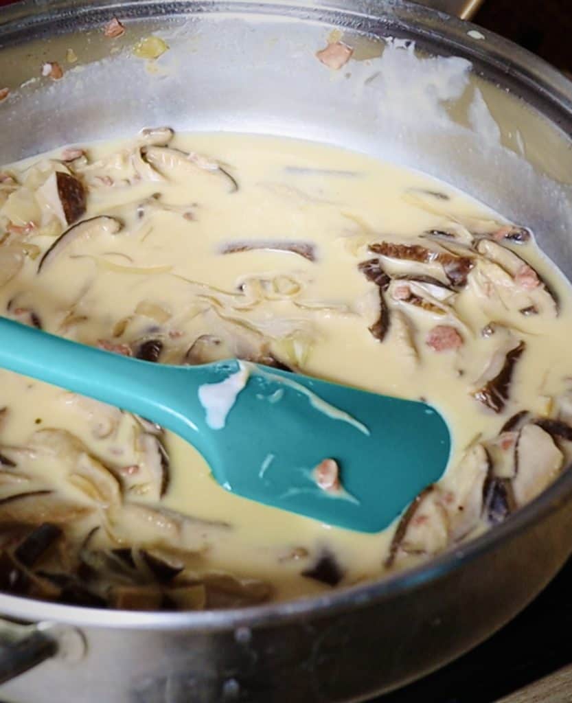shiitake and onion slices swimming in a milky broth with a blue spatula