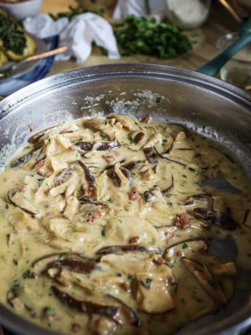 a stainless steel pan full of marsala cream sauce with shiitake mushrooms