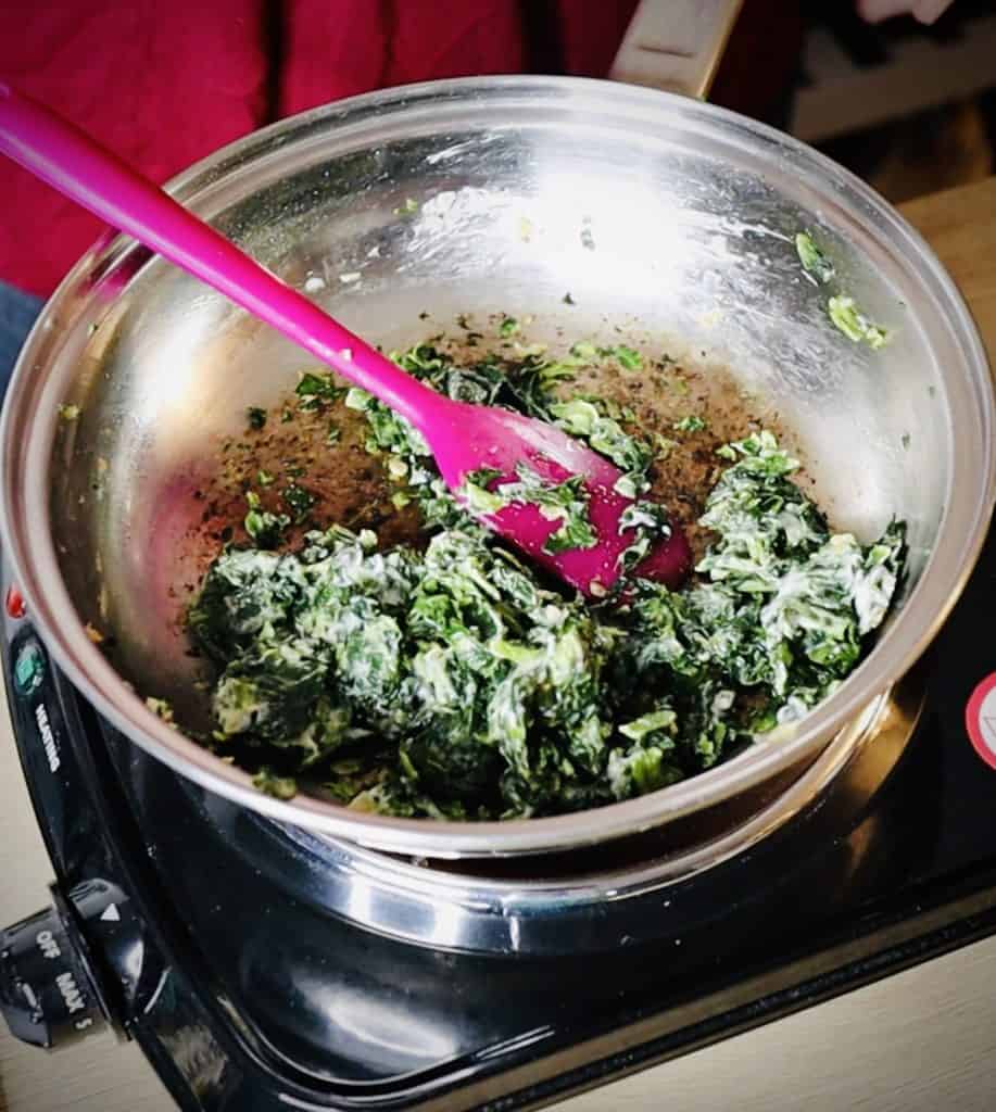 Deep green spinach with streaks of creamy white through it in a stainless steel saute pan