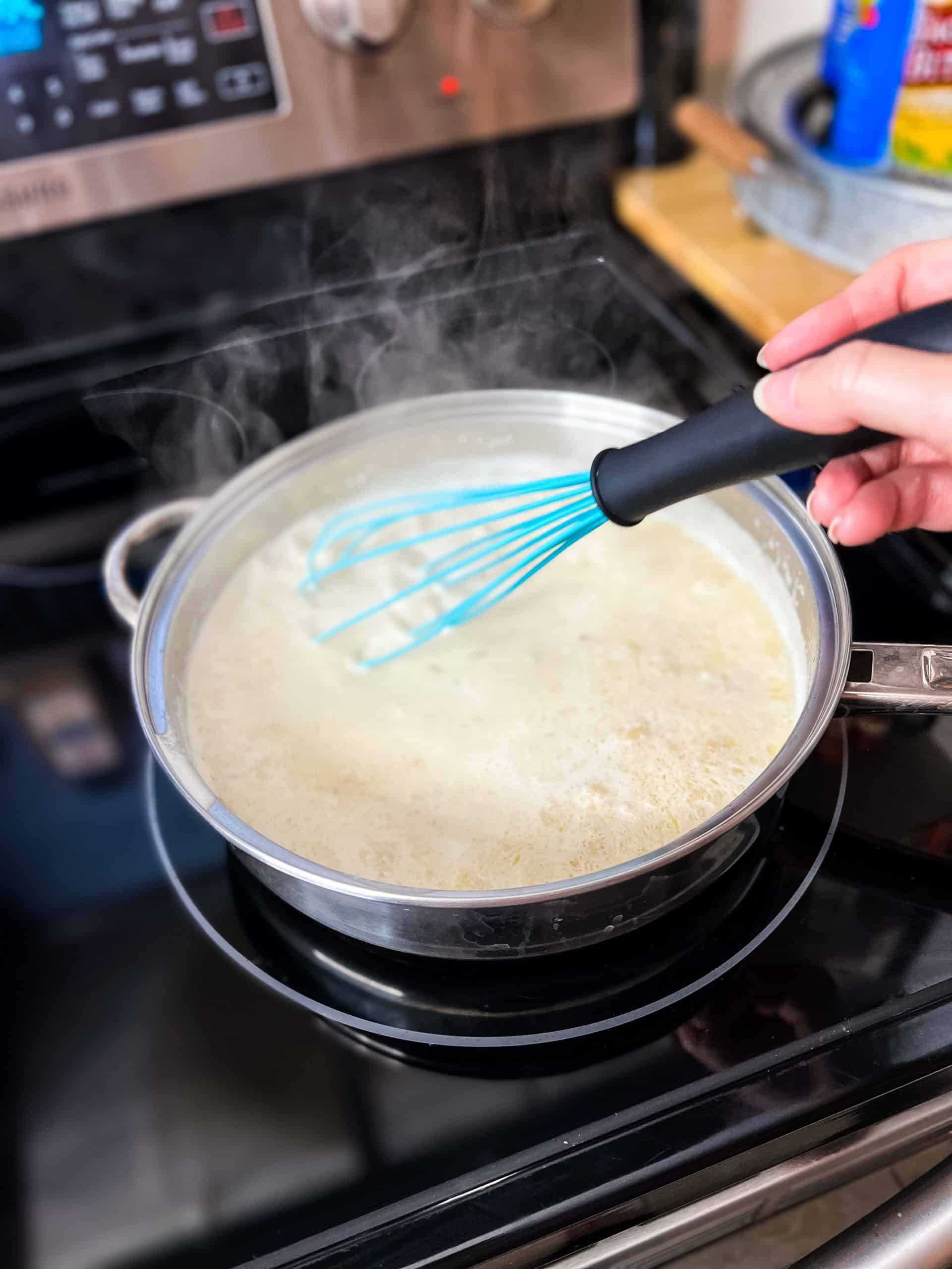 a turquoise colored whisk stirring together milk and melted butter in a stainless steel pan