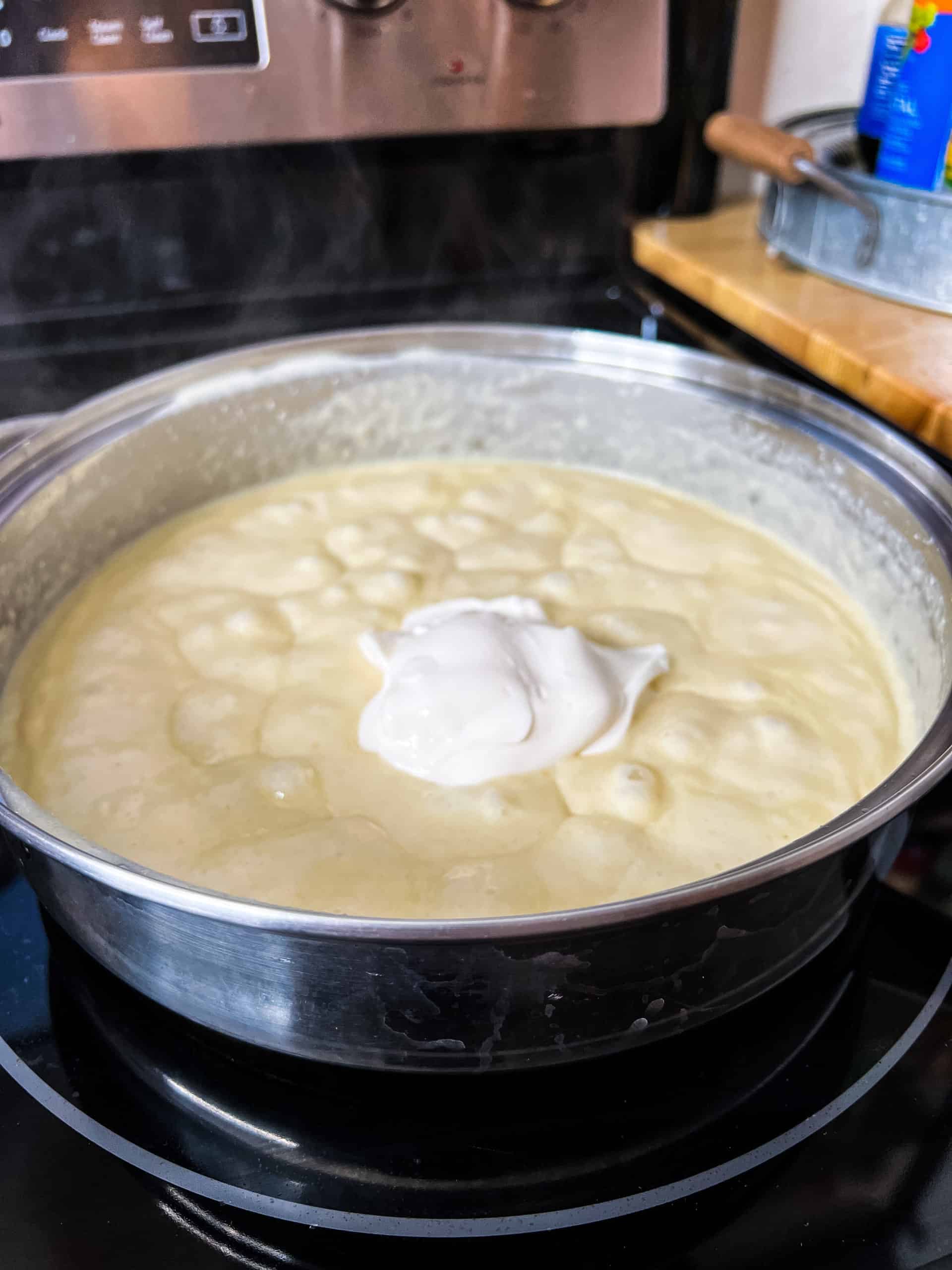 a dollop of mayonnaise on top of Alfredo sauce in a stainless steel pan