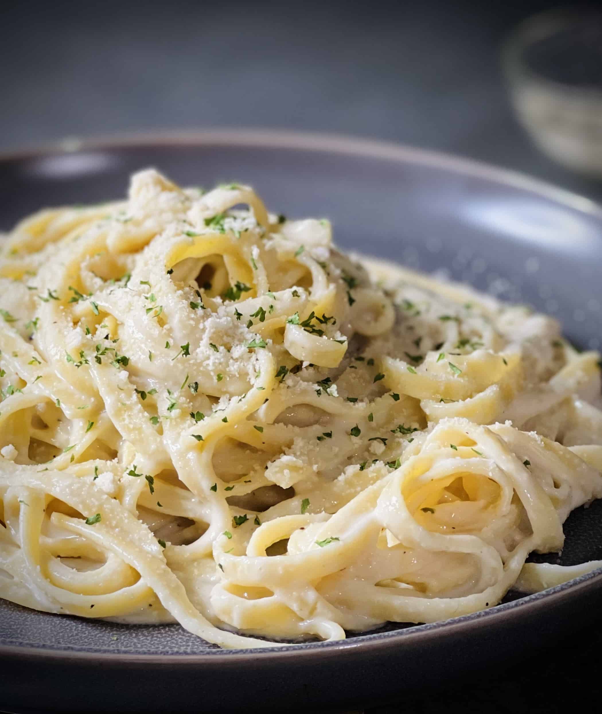 pile of fettuccini Alfredo on a grey plate with a grey countertop underneath