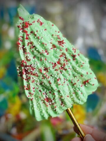 A pastel green Christmas tree shaped meringue cookie with red and white sprinkles and a gold stick